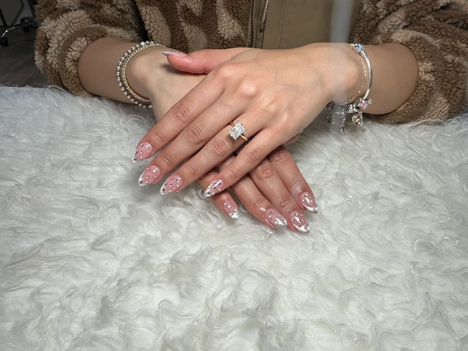 Almond nails in a soft pink with clear tips and scattered rhinestones, resting on white fur