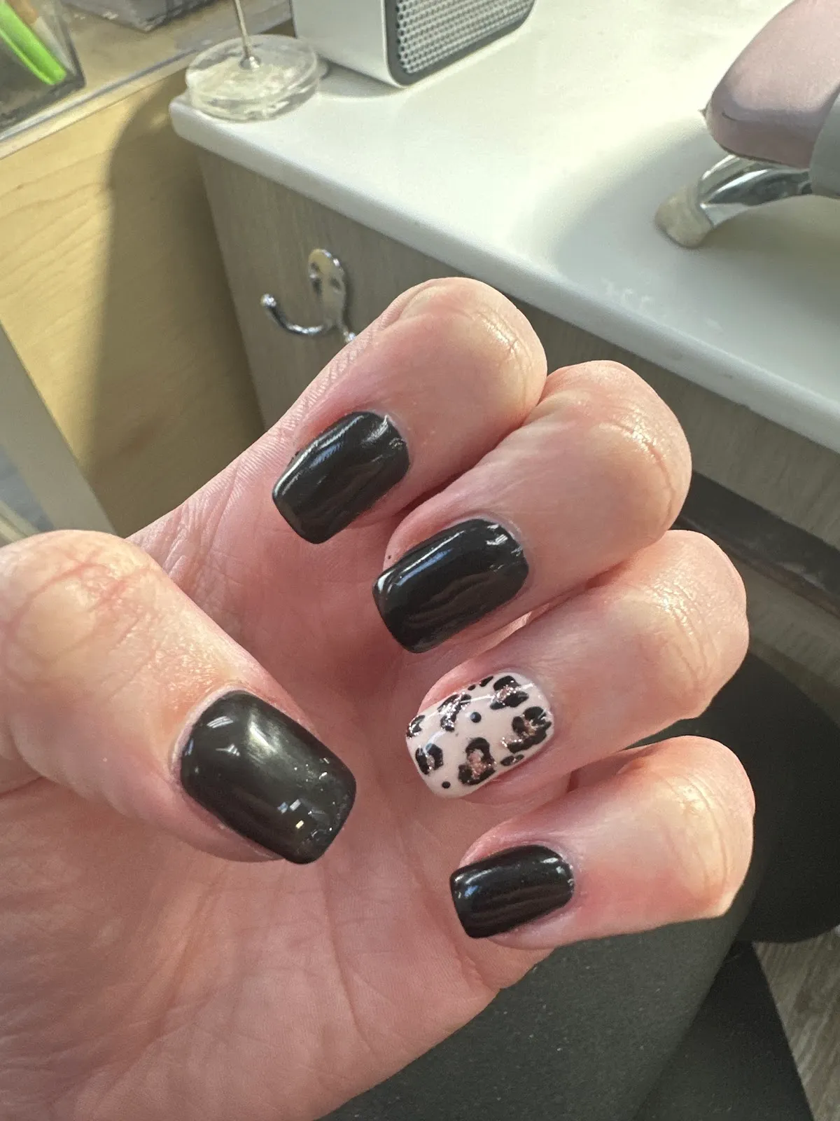 Glossy black gel nails with a single leopard-print accent nail